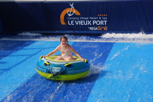 Fillette sur une bouée tractée du simulateur de vagues du camping 5 étioles Le Vieux Port dans les Landes