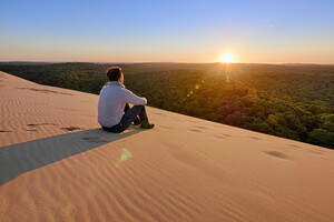 Alors que le soleil commence à descendre lentement vers l'horizon, la dune du Pilat se pare de teintes dorées et orangées. Les grains de sable, chauds sous les pieds, scintillent comme des milliers de petits joyaux, tandis qu'une brise légère souffle, apportant avec elle les parfums résineux de la forêt des Landes qui s'étend à perte de vue.