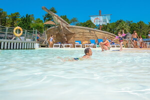 Enfant s'amusant gaiement dans l'eau chauffée de la pataugeoire du parc aquatique du camping 5 étoiles dans les Landes en bord de mer