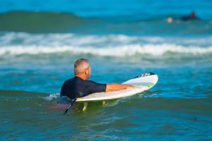 Camping avec accès direct à la plage en bord de mer (10) un homme apprend à surfer et va avec sa planche plus loins dans l'océan pour la vague