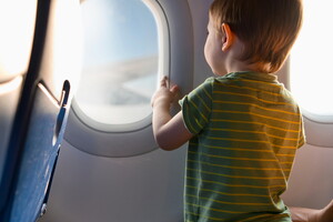 Un bambin regardant à travers le hublot d'un avion, illustrant le voyage vers un camping en pleine nature.