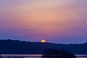 Un spectaculaire coucher de soleil illuminant l'étang noir de Seignosse, avec des teintes chaudes d'orange et de violet se reflétant sur l'eau calme, entouré d'une végétation verdoyante et d'une ambiance paisible.